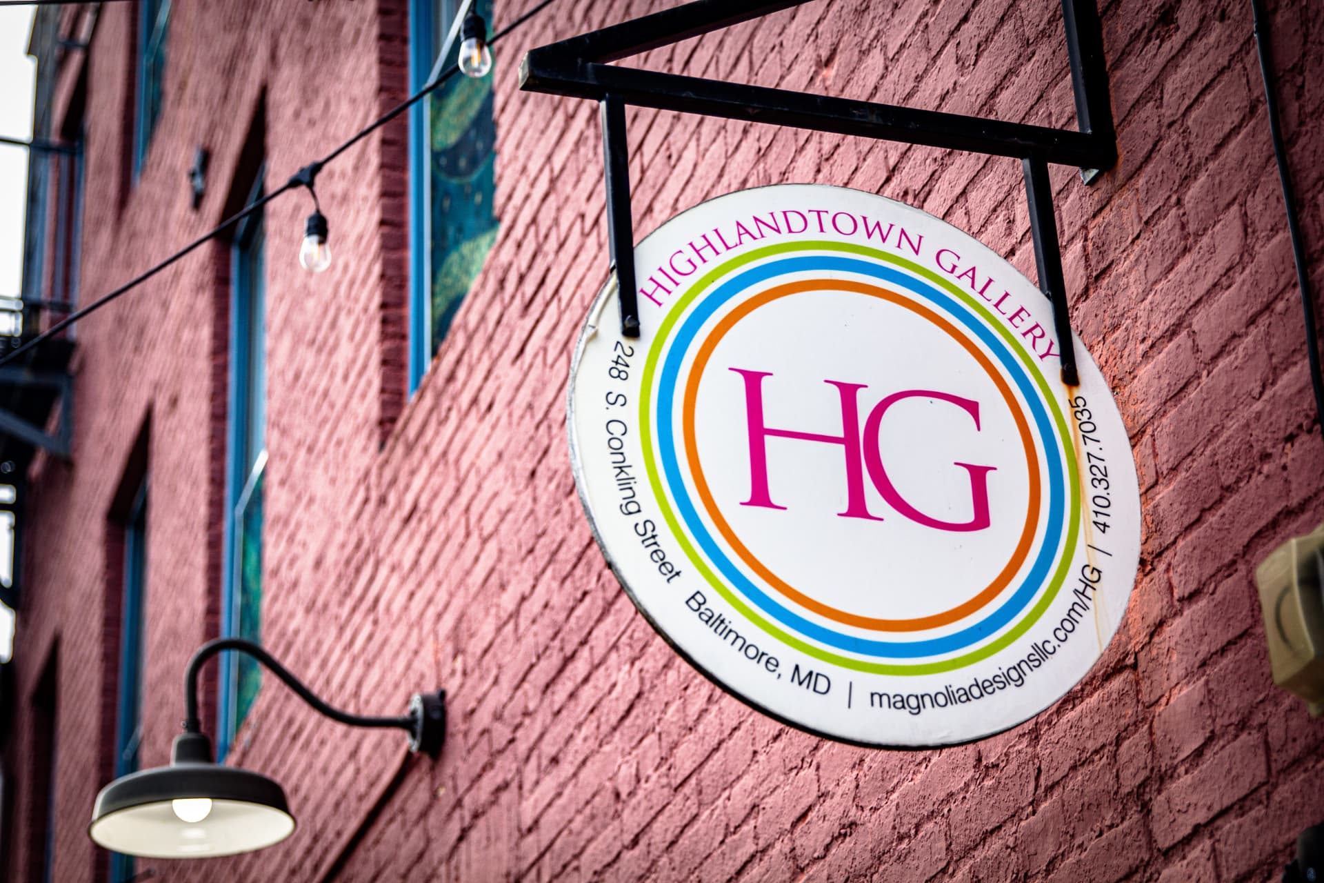 Highlandtown Gallery hanging sign on a pink brick wall